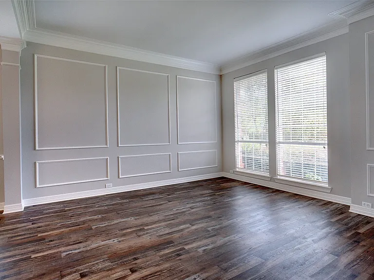 Room featuring wood-finish flooring, decorative wall molding, crown molding, and two tall windows with blinds