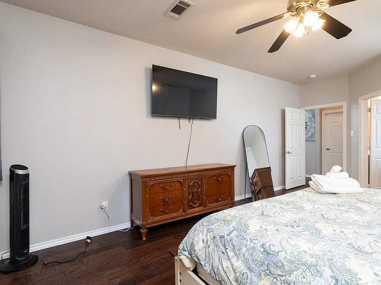 Relax in the primary bedroom with a king bed, soft bedding, TV, and warm lighting. Features a ceiling fan, dresser, room-darkening curtains, and a private attached bathroom for added comfort.