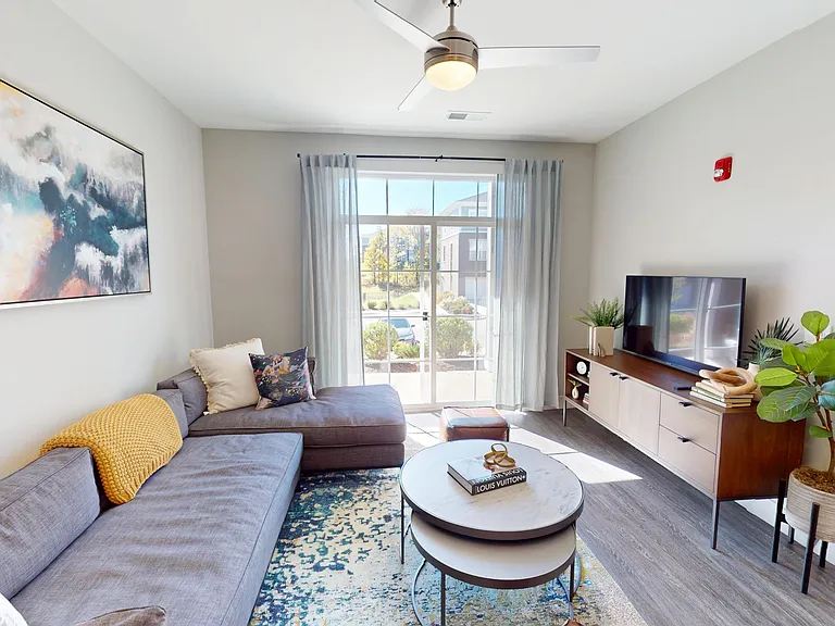 The Oaks floor plan features a large living room with wood-style flooring and a sliding glass door to a private patio or balcony. The Oaks floor plan features a large living room with wood-style flooring and a sliding glass door to a private patio or balc