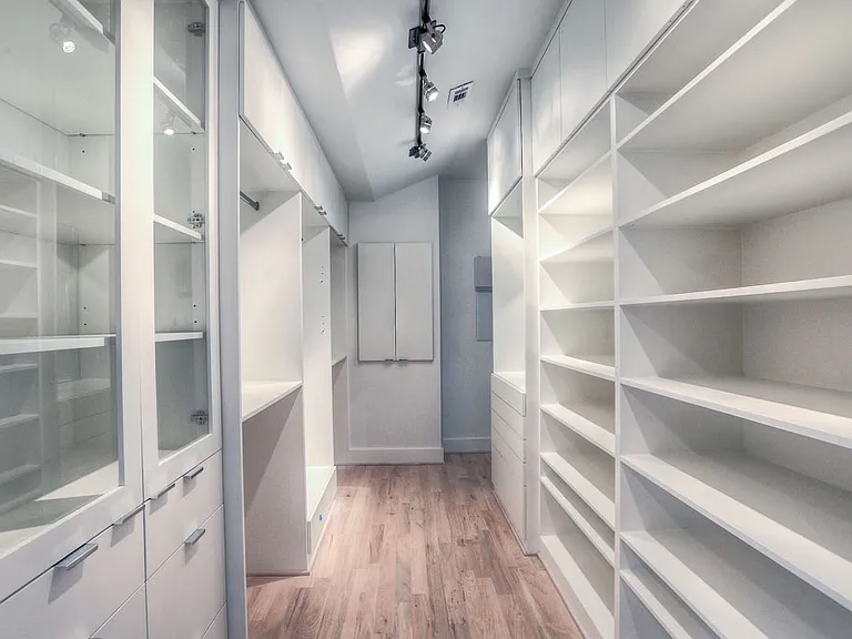 Walk-in closet with custom built-ins, glass display cabinets, open shoe shelving, vaulted ceiling, and track lighting