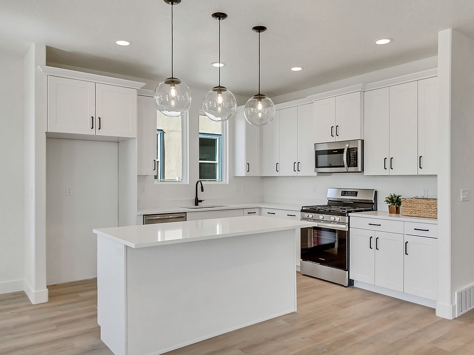 Modern kitchen with white cabinets, island, and stainless steel appliances. Three pendant lights han
