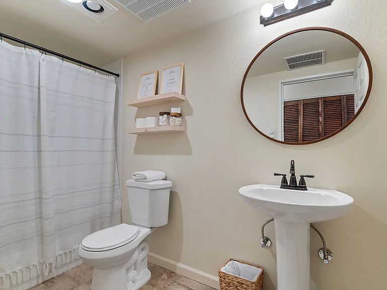 This first floor bathroom has no cabinets but a small wall mounted shelf is located next to the sink and one small shelf is mounted inside the bathtub enclosure.