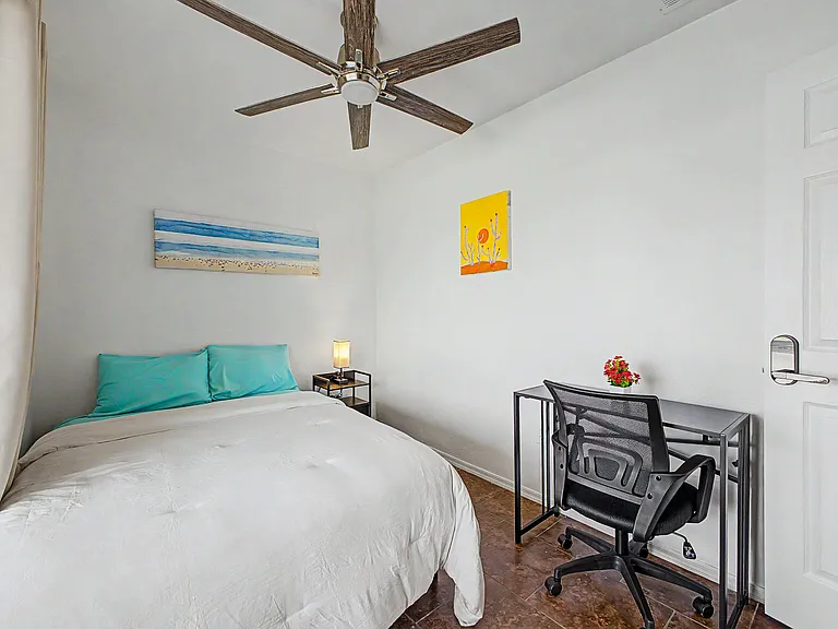 Furnished bedroom with ceiling fan, nightstand lighting, and a dedicated desk workspace for studying or remote work.