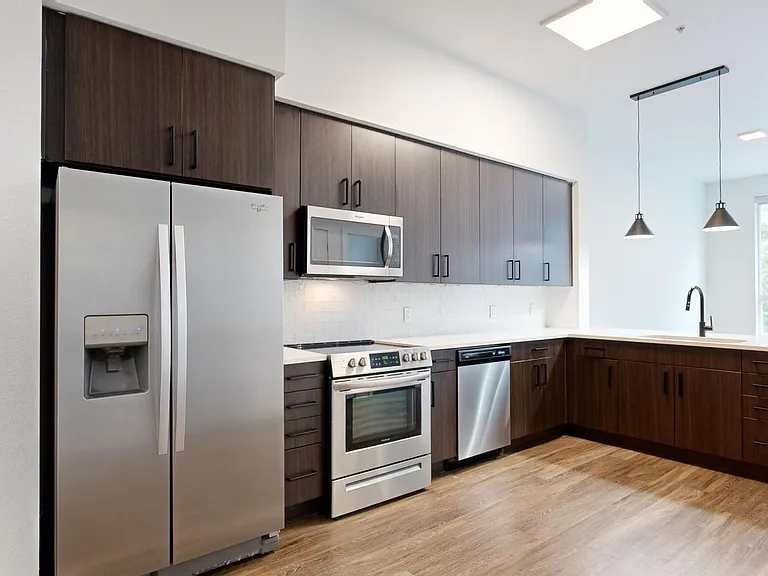 Apartment kitchen with stainless steel appliances, quartz countertops, and wood-style flooring.