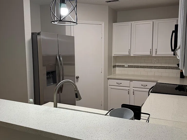 Functional kitchen with ample cabinet storage, generous countertops, and stainless-steel refrigerator for daily meal prep.