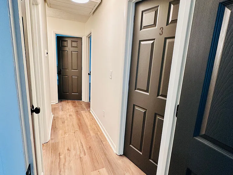 Clean, well-lit hallway with durable wood-look flooring and multiple doors for easy access to bedrooms and shared areas.