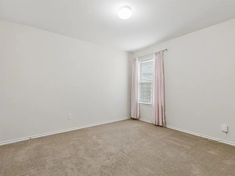 Neutral-toned room featuring a single window with blinds, light-colored walls, and carpet flooring