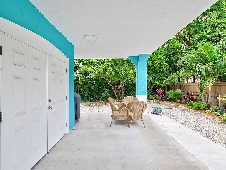 Private Laundry room and small storage area under carport with french doors and fully landscaped shared backyard shrubs and trees
