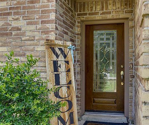 A lineage of cycas palm tree plants to your left and lush grass to the right lead you to the entryway where a wooden door with in-laid glass welcomes you.