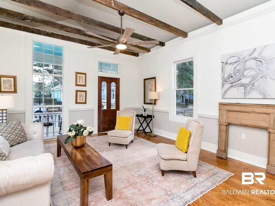 Living area featuring a wainscoted wall, beamed ceiling, wood finished floors, and a ceiling fan
