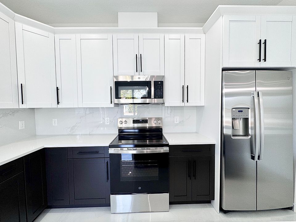 The spacious open kitchen features quartz countertops, stainless steel appliances, soft-close cabinets, a large island, and modern pendant lighting.
