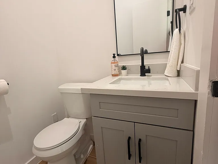 Compact bathroom with a single-sink vanity, ample cabinet storage, and a large mirror with matte-black fixtures.