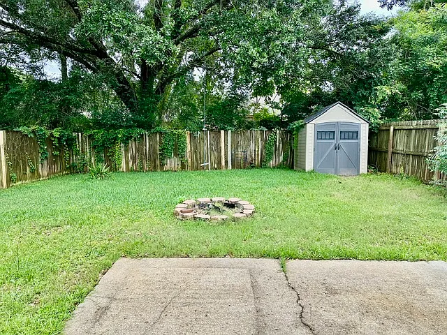 Fenced in backyard with patio, brick fire pit, and shed
