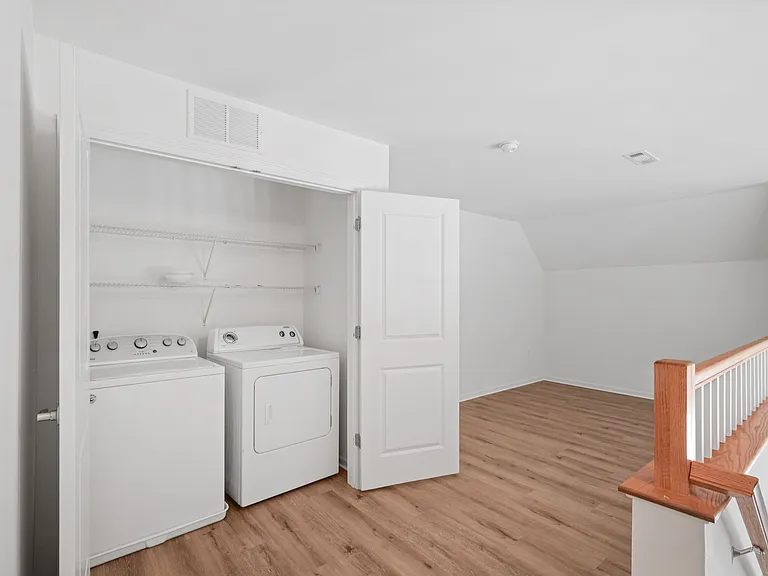 Bright laundry area with modern washer and dryer, featuring elegant wooden flooring and ample shelving space.