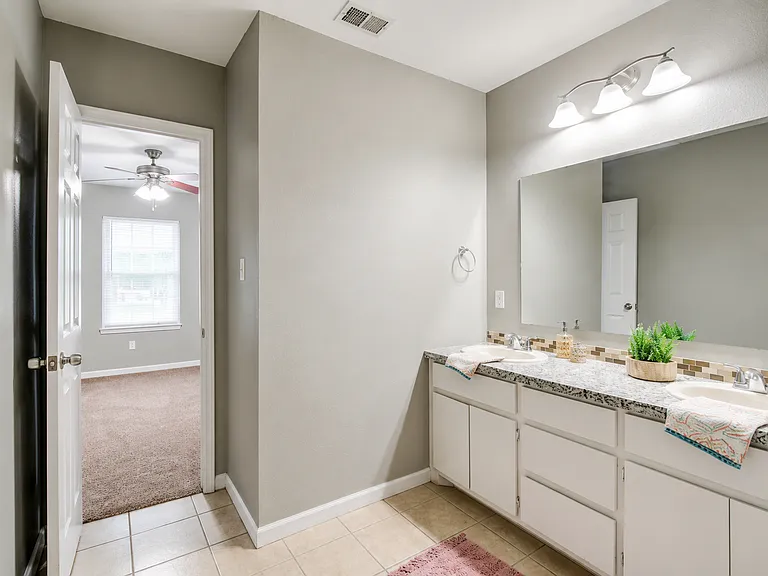 Shared Jack & Jill bathroom connecting Suites 1 & 2. Features a double-sink vanity with ample counter and cabinet space, bright lighting, and a full bathtub with shower. Each bedroom has its own private entrance for added convenience.