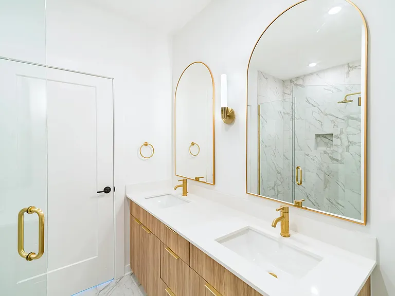 A bright primary bath at Modera Nations in Nashville pairs sleek double vanities, warm brass accents, and refined finishes for a polished daily routine.