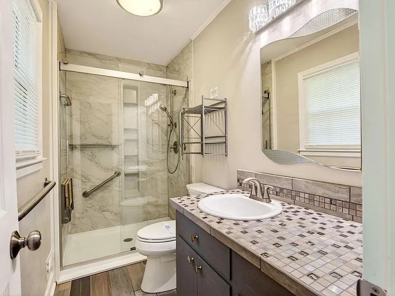 Updated full bath with glass-enclosed shower, built-in shelving, and a wide vanity with ample counter space and storage.