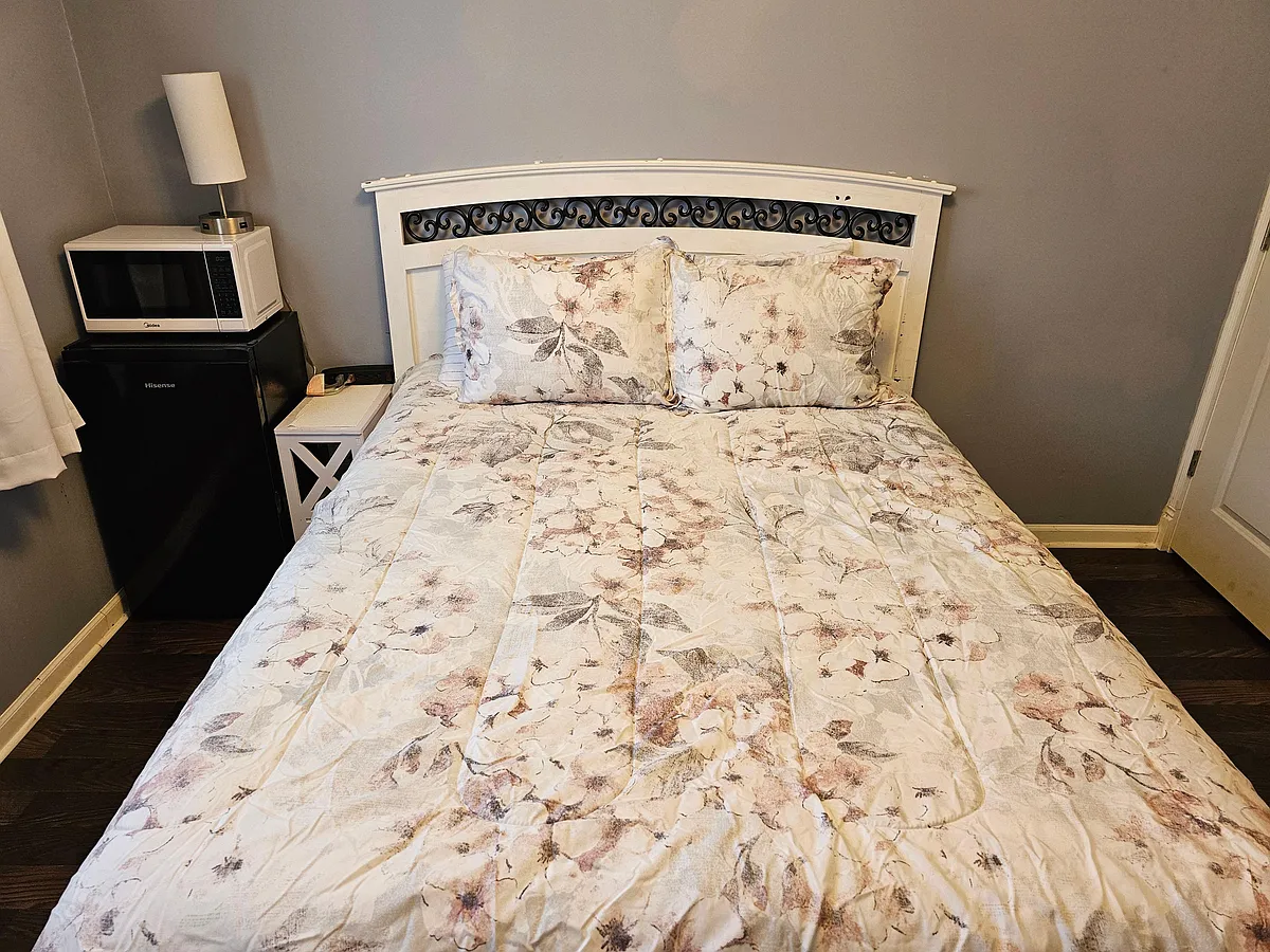 Furnished bedroom with a full bed, nightstand lighting, and in-room mini fridge with microwave for added convenience. - Navarre Rd