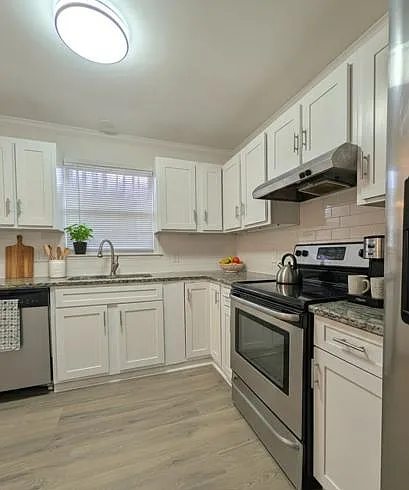 L-shaped kitchen with ample white cabinetry, granite-look counters, stainless appliances, and a window over the sink.