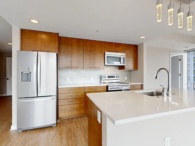 Apartment kitchen with stainless steel appliances, quartz countertops, and wood-style flooring.