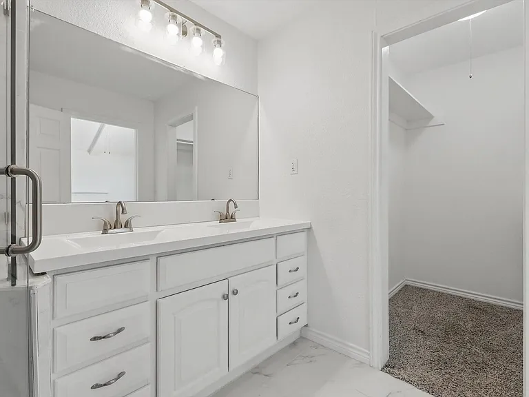 Bathroom featuring double vanity, a spacious closet, marble finish floors, and baseboards