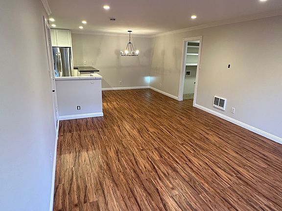 Living room showing recessed lighting, crown and base board moldings (throuout the unit), LVP flooring, and the kitchen on far left.