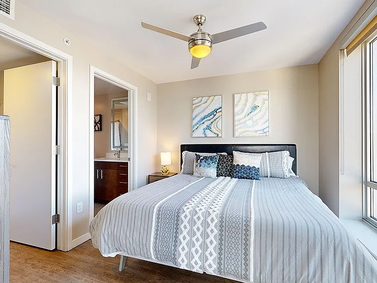 Spacious apartment bedroom with large closet, attached bathroom and wood-style flooring.