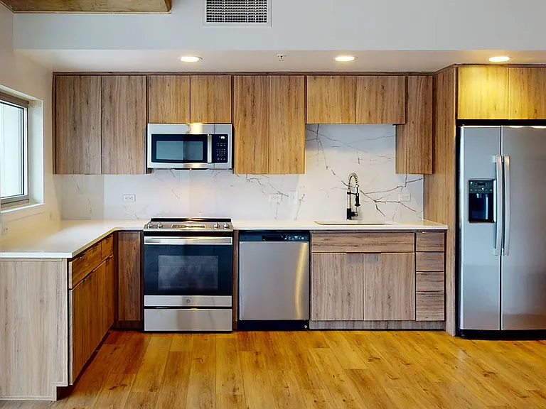 Apartment kitchen with stainless steel appliances, quartz countertops and wood-style flooring.
