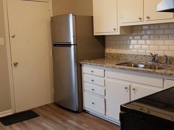 View of the kitchen which includes stainless steel appliances, granite counter tops, subway tile backsplash, and luxury vinyl plank (LVP) flooring. There is a door to access the rear of the building and off street parking areas.