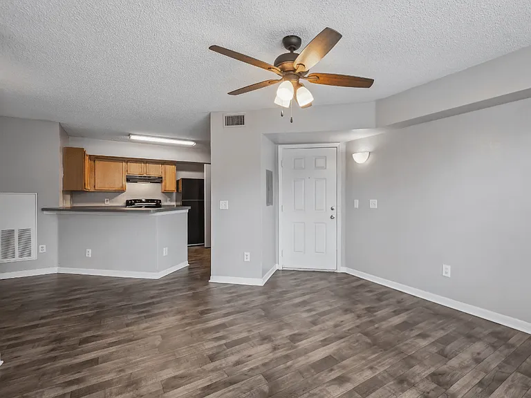 Open-concept living room with wood-style flooring, breakfast bar, ceiling fan, and kitchen in a 1-bedroom apartment home at Gregory Cove in Jacksonville, FL.