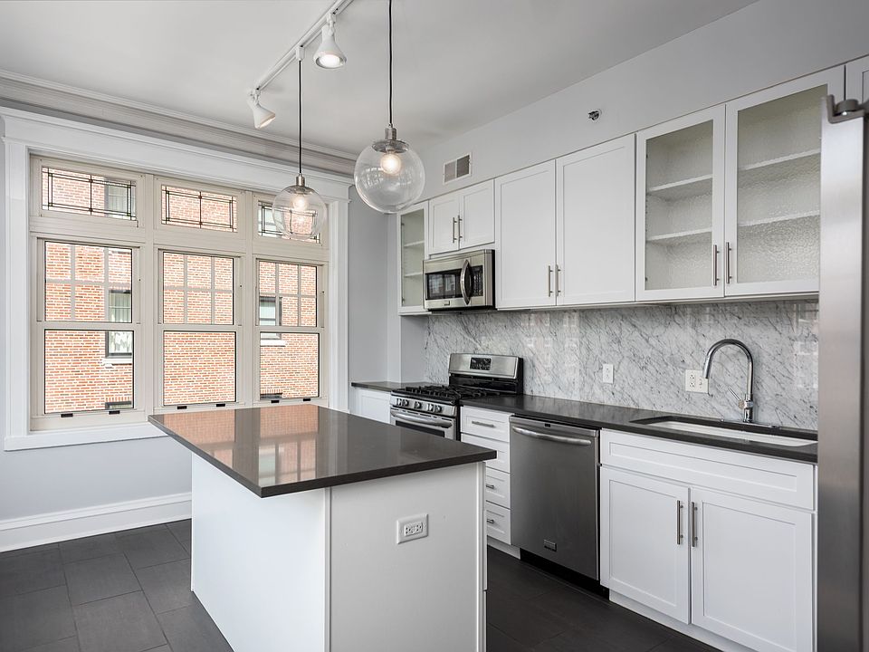 York House designer kitchen with gas stove, quartz countertops, stainless steel appliances, marble kitchen backsplash, and slate tile floor.