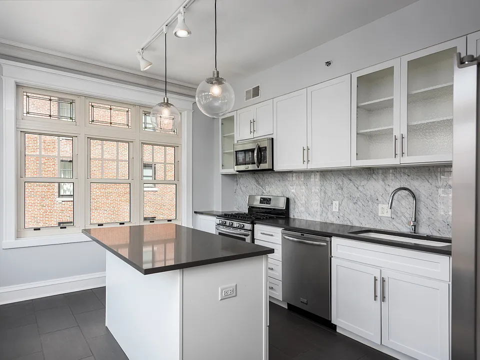 York House designer kitchen with gas stove, quartz countertops, stainless steel appliances, marble kitchen backsplash, and slate tile floor.