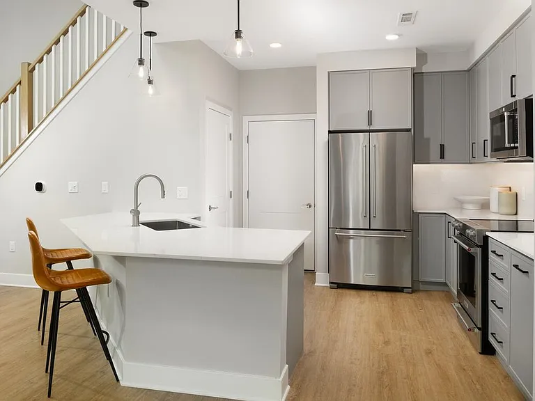 Signature Collection Townhome kitchen with upgraded stainless steel appliances, white quartz countertops and backsplash, grey cabinetry, hard surface flooring, and pendant lighting.