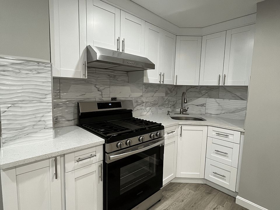 Modern, fully renovated kitchen featuring sleek white cabinetry, stainless steel range hood, high-end appliances, and stylish backsplash. Elegant flooring and bright recessed lighting complete this stunning space!