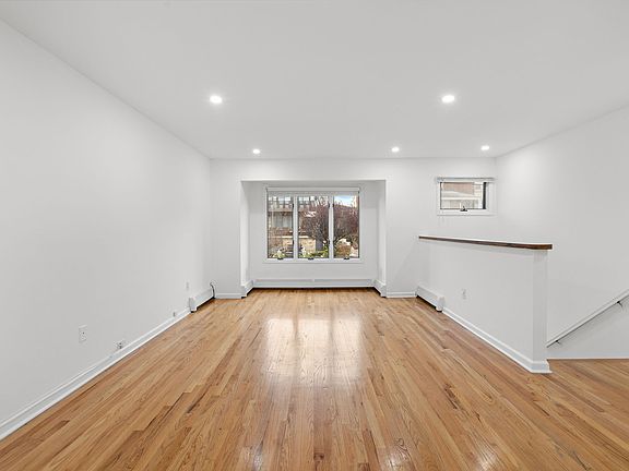 This grand living room is flooded with natural light, creating an inviting space perfect for both relaxation and entertaining. Gleaming hardwood floors and recessed lighting add a touch of sophistication, complementing the room's generous proportions.