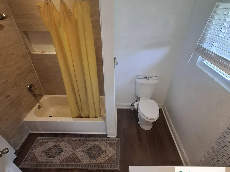 Full bathroom with tub/shower combo, tile surround, window with blinds, and durable flooring for easy upkeep.