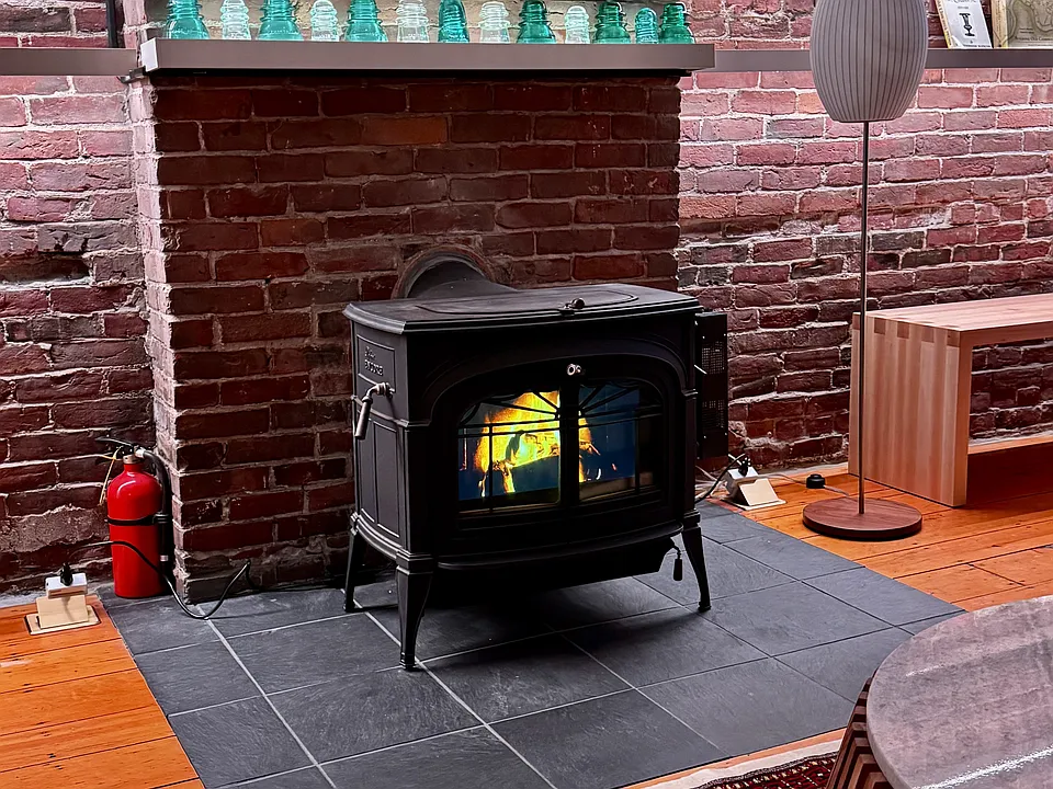 Living room _ Vermont Castings vintage stove projecting digital fire, brick chimney breast, antique glass insulators on the mantel.