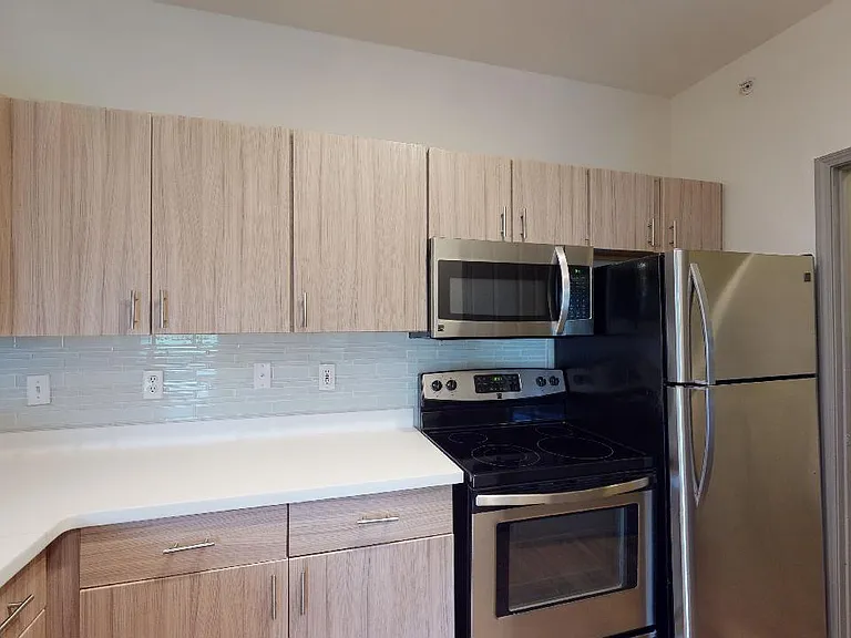 Apartment kitchen with stainless steel appliances, quartz countertops and wood-style flooring.