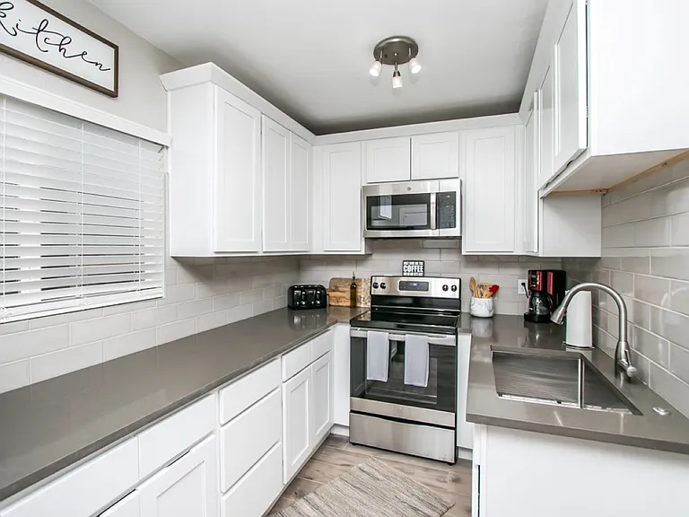 Detached casita kitchen at, Tempe rental home. Features modern white shaker cabinets, stainless steel appliances, grey quartz countertops, a matching subway tile backsplash, and a deep undermount sink. Fully equipped kitchen for a top Tempe, AZ stay.