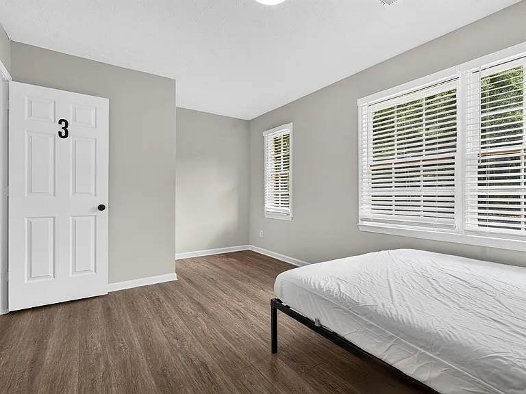 Private bedroom with wood-style flooring, neutral walls, and large windows with blinds for natural light and privacy.
