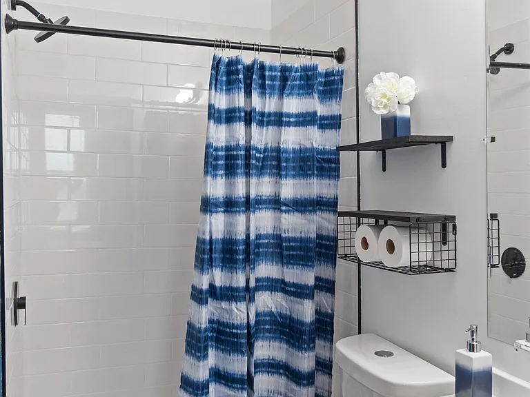 Bathroom with tiled tub/shower combo, vanity sink, mirror, and convenient wall shelving for everyday storage.