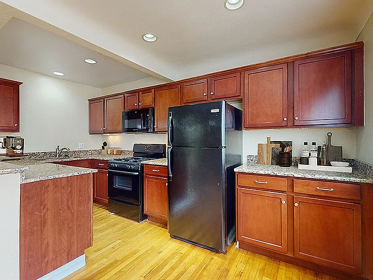 Modern kitchen with rich wooden cabinetry, granite countertops, and sleek black appliances, offering a warm and inviting cooking space.
