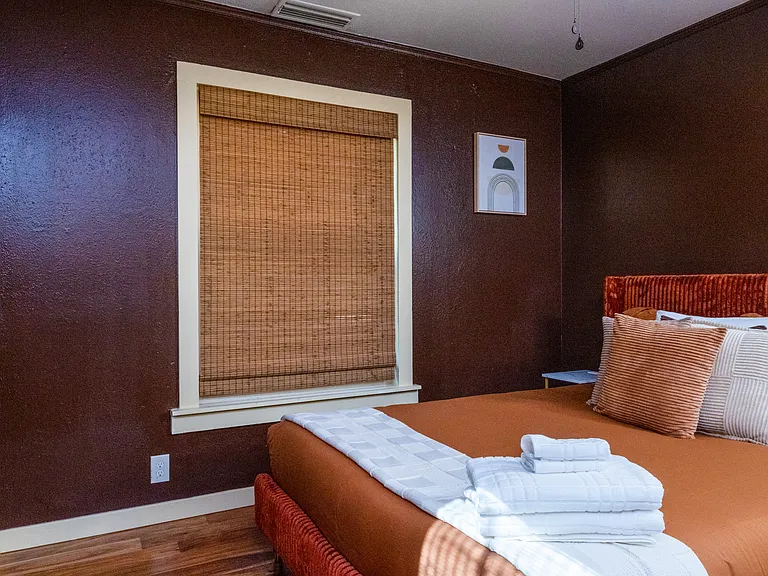 Cozy retreat with warm tones and natural light. This comfortable bedroom features a queen bed, bamboo shades, a ceiling fan, and a modern mirror accent _ perfect for unwinding after a day exploring Dallas.