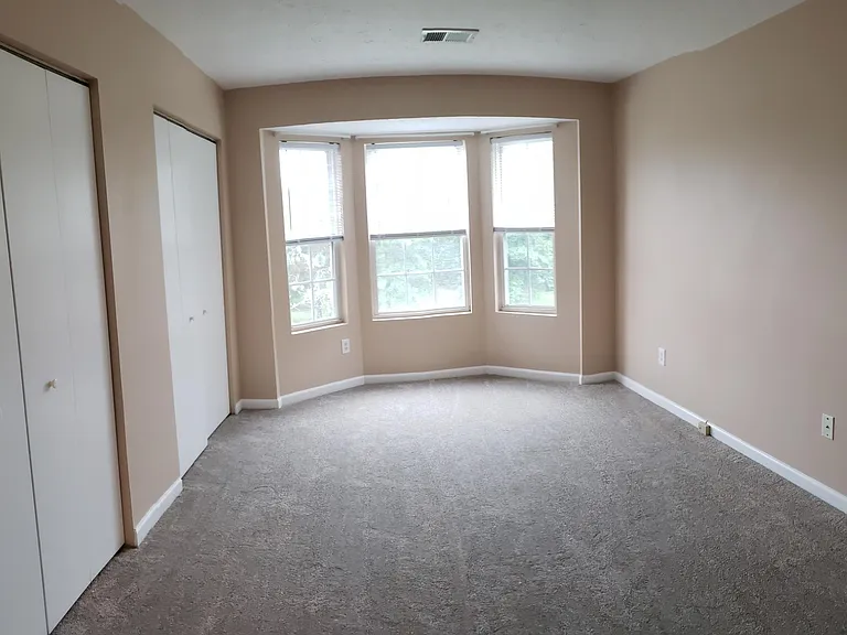 Large 2nd bedroom with bay window overlooking private grassy area with trees.