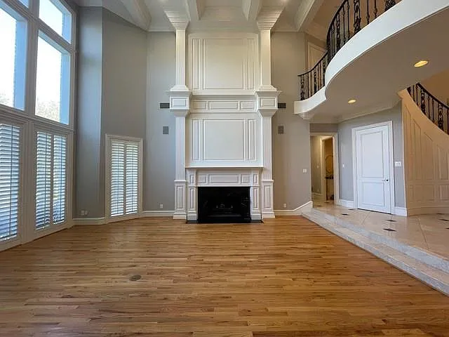 Unfurnished living room featuring light wood-type flooring, a towering ceiling, a fireplace with flush hearth, healthy amount of natural light, and stairway