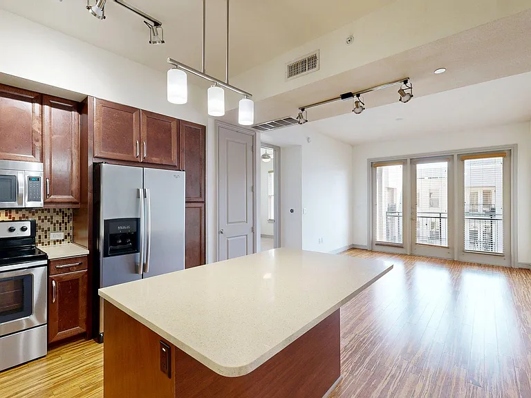 Apartment kitchen with stainless steel appliances, light counters, and wood style floor.