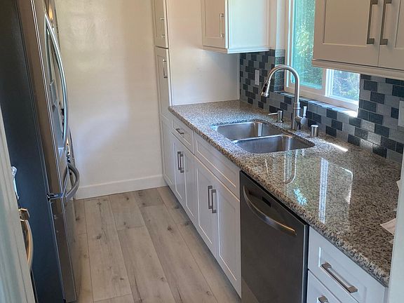 White shaker cabinets, stainless steel dishwasher, attractive view of nature from kitchen window.