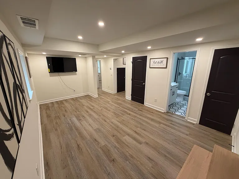 Open common area with durable plank flooring, recessed lighting, and wall-mounted TV, with easy access to nearby rooms.