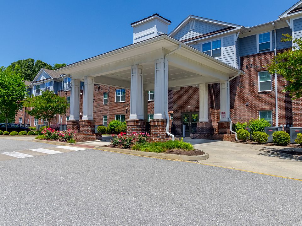 Spacious front entrance highlighted by tall white columns, brick detailing, and flower-filled garden beds at Snowden Senior Apartments.