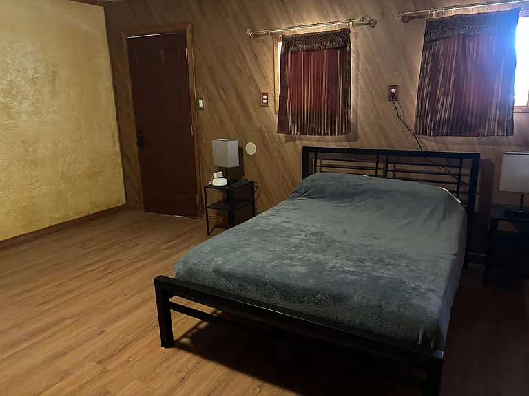 Private bedroom with a metal bed frame, nightstands with lamps, and two windows with curtains for light and privacy.